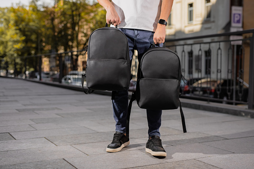 Two black leather backpacks holding male hands in city
