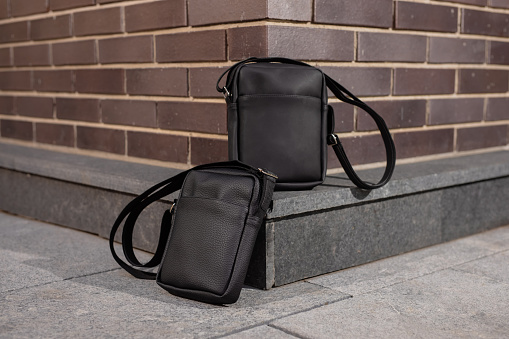 Two black leather messenger bags near brick wall background