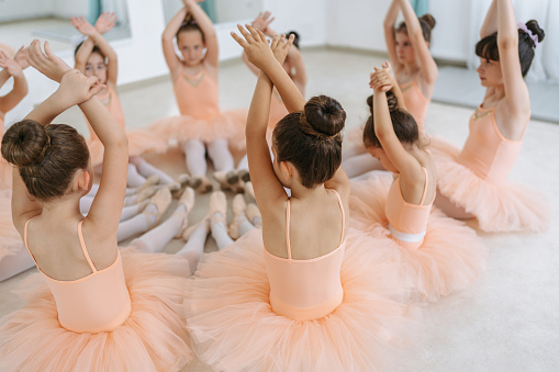 Photo of cute little ballerinas sitting on the floor and warming up or a ballet class.