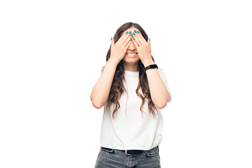 Photo of laughing young woman covering her eyes with her hands over a white studio background