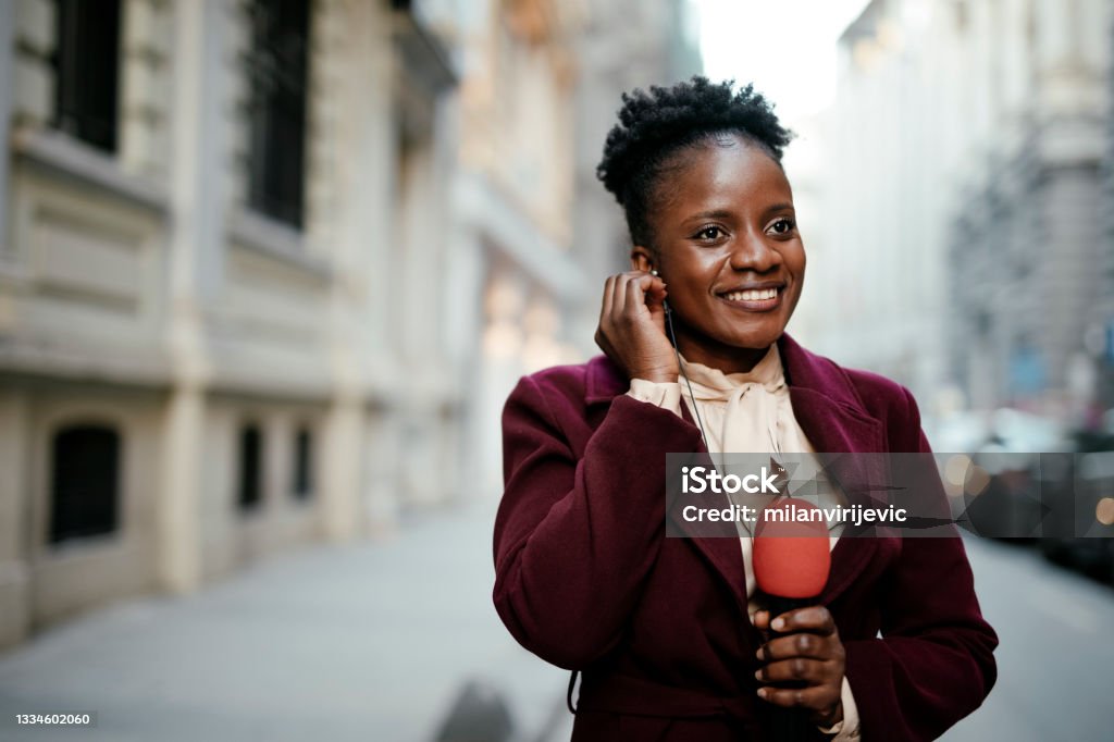 African female news reporter in live broadcasting. Young African journalist using a microphone at the city. African female news reporter in live broadcasting. Journalist Stock Photo