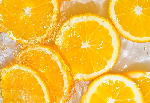 Slices of oranges in water on white background. Oranges close-up in liquid with bubbles. Slices of juicy ripe oranges in water. Macro image of fruits in water.