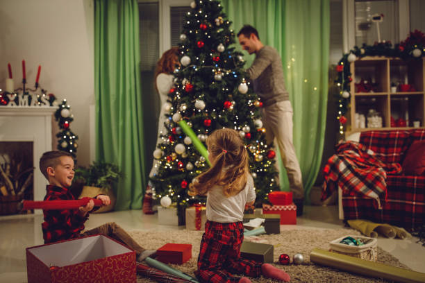 istock Kids playing with wrapping paper rolls while parents are decorating the Christmas tree 1334609634