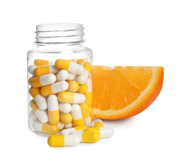 garrafa com pílulas de vitamina e laranja no fundo branco - vitamin pill nutritional supplement capsule antioxidant - fotografias e filmes do acervo