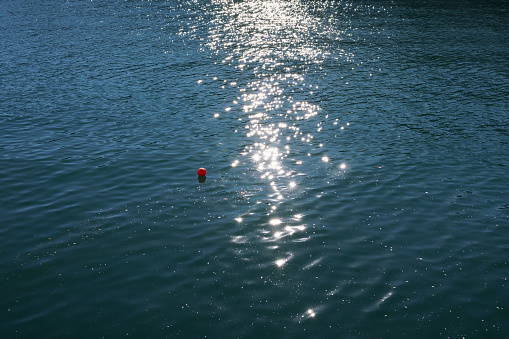 Sunlight reflecting past a small red ball floating in the ocean.