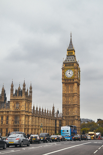 London, UK - May 6, 2014: An iconic double decker red London bus drives past Big Ben and over the Westminster Bridge 