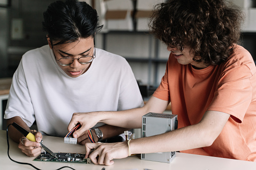 Dos amigos estudiantes de secundaria soldando juntos dispositivo de placa de circuito electrónico en el taller de tecnología científica - Innovación digital en la educación photo