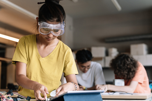 Niña estudiante asiática con gafas protectoras que aprenden tecnología, robótica y electrónica en la escuela secundaria photo