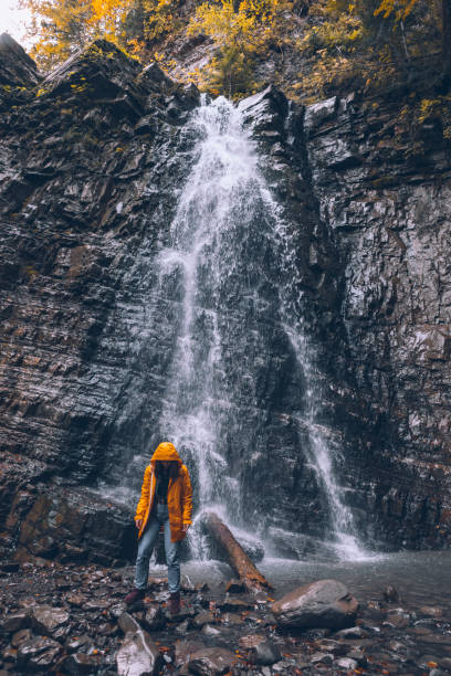 istock woman in yellow raincoat at autumn waterfall 1334626867