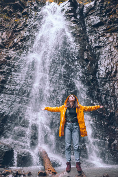 istock woman in yellow raincoat at autumn waterfall 1334626890