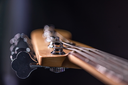Detail of a tuning post on the wooden headstock of an electric bass guitar.