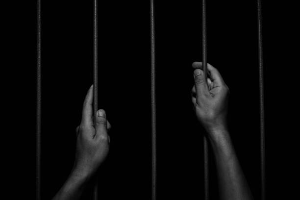 istock Man Hands holding iron bars in jail. Imprisoned criminal concept. 1334628288