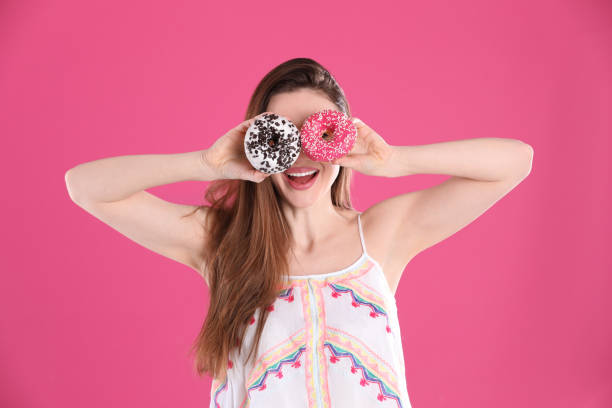 istock Beautiful young woman with donuts on pink background 1334628328