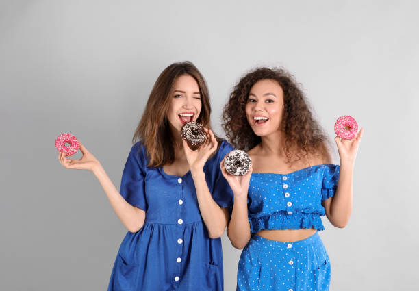 istock Beautiful young women with donuts on light grey background 1334628349