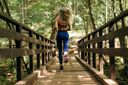 Beautiful woman exercising outdoors and running over wooden bridge in natural park. She is very attractive and she wears sportswear