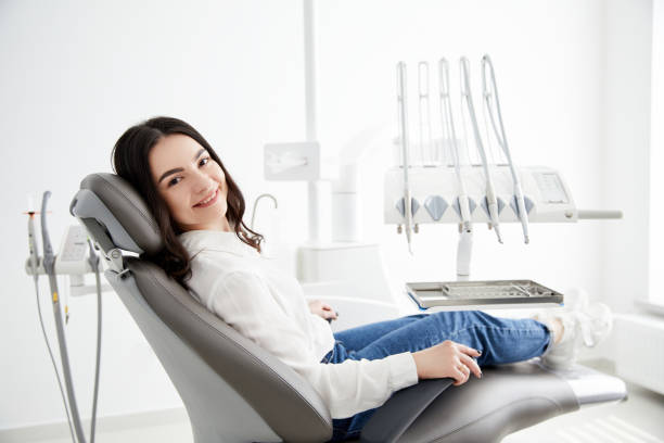 Image of satisfied young woman sitting in dental chair at medical center while professional doctor Image of satisfied young woman sitting in dental chair at medical center while professional doctor fixing her teeth dentists chair stock pictures, royalty-free photos & images