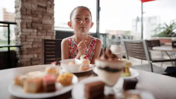 Photo of Girl eating a lot of sweets at a restaurant