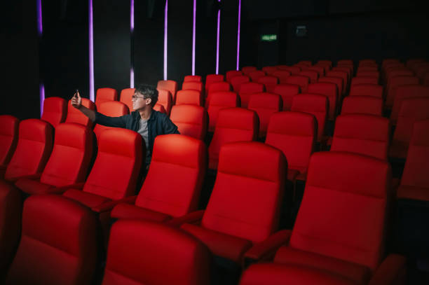 istock asian chinese young man taking selfie with smart phone vlogging  enjoying himself alone while waiting for movie show time in movie theater cinema posting to social media 1334635182