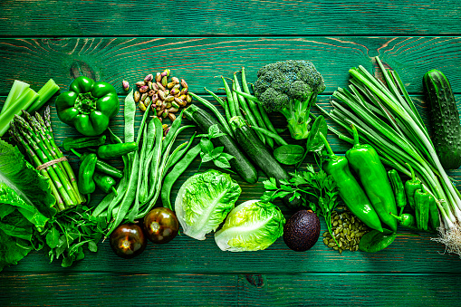 Healthy eating concepts: green table filled with a large number of green vegetables arranged in a row shot from above. The composition includes broccoli, lettuce, zucchini, tomato, spinach leaves, green bell pepper, green beans, asparagus, avocado, cucumber, zucchini, parsley, pistachio and pumpkin seeds among others. High resolution 42Mp studio digital capture taken with SONY A7rII and Zeiss Batis 40mm F2.0 CF lens