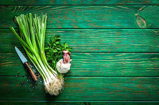 Cooking backgrounds. Fresh scallion bunch, parsley, garlic, salt and pepper arranged at the left of an horizontal green table leaving useful copy space for text and/or logo at the right. A kitchen knife complete the composition. High resolution 42Mp studio digital capture taken with SONY A7rII and Zeiss Batis 40mm F2.0 CF lens