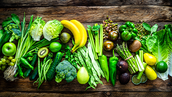Healthy eating concepts: wooden table filled with a large number of green fruits and vegetables arranged in a row shot from above. The composition includes broccoli, lettuce, pear, banana, kiwi fruit, zucchini, tomato, spinach leaves, grape, lime, green bell pepper, green beans, asparagus, avocado, parsley, pistachio and pumpkin seeds among others. High resolution 42Mp studio digital capture taken with SONY A7rII and Zeiss Batis 40mm F2.0 CF lens