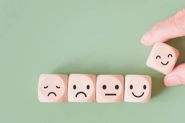 hand selected happy face wood cube and others on green background for customer service evaluation, feedback, satisfaction survey or mental heath concept stock photo