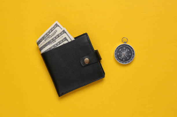 Leather wallet with one hundred dollar bills and compass on yellow background