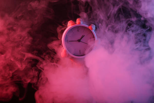 Hand holding clock in dense smoke with red-blue neon light.