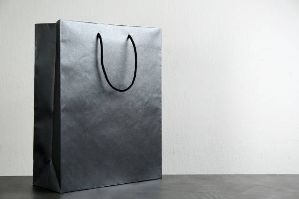 istock Black shopping paper bag on table against light background. Space for text 1334639863