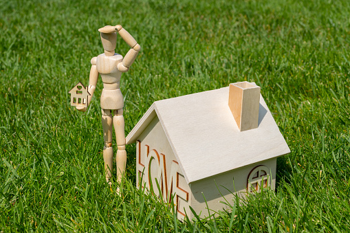 Figurine of a wooden person and symbolic wooden houses on a background of green grass