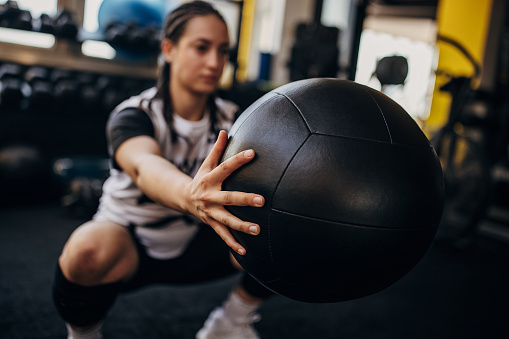 One woman, young woman exercising with medicine ball in gym alone.