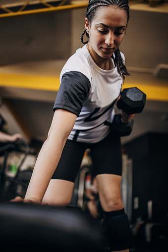 One woman, young woman exercising with dumbbell in gym alone.