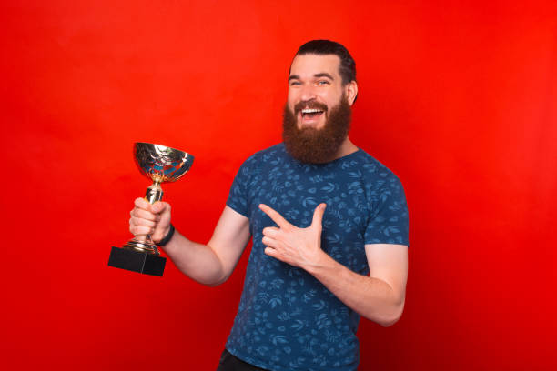 istock Joyful man is holding a trophy and pointing at it over red background. 1334643894
