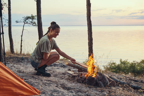 istock Female hiker throwing log into campfire outdoor 1334645561