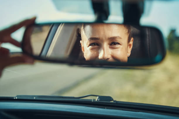 glückliche frau, die ihr gesicht im rückspiegel betrachtet - rear view mirror car mirror rear view stock-fotos und bilder