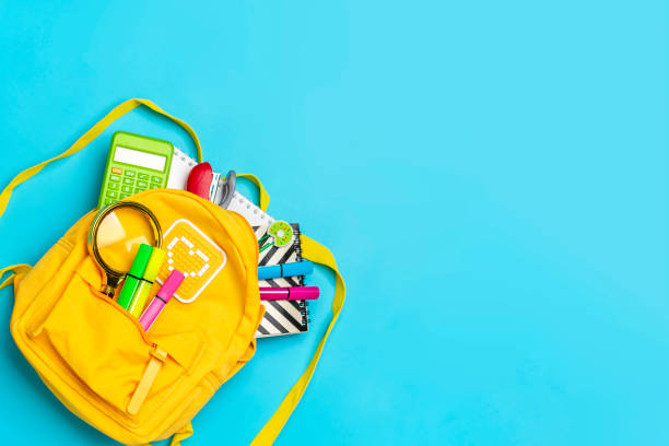 istock Back to school, education concept. Yellow backpack with school supplies - notebook, pens, ruler, calculator, scissors isolated on blue background. Top view. Copy space Flat lay composition 1334647235