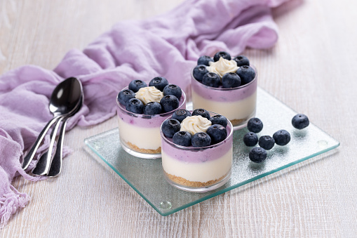 Blueberry cheesecake topped with whipped cream in a glass on a white wooden table