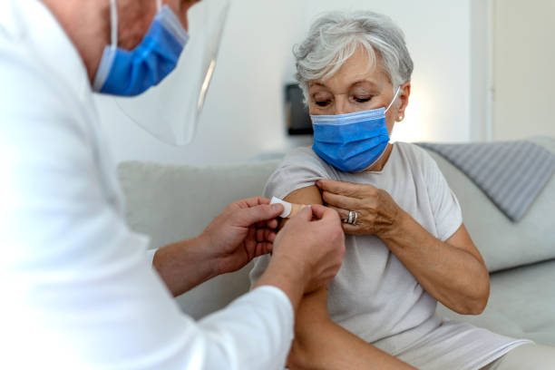 un médecin de sexe masculin pose un pansement sur le bras d’une femme âgée après qu’il a administré l’injection du vaccin contre la covid-19. - injecting flu virus cold and flu doctors office photos et images de collection