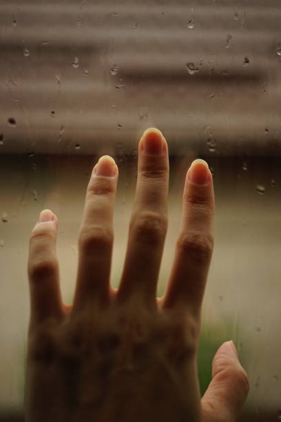 istock Hand touches a window in rain drops 1334649820