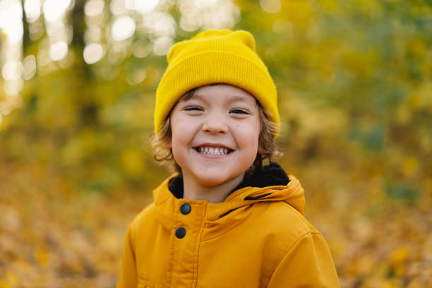 um garotinho de chapéu amarelo e jaqueta caminha pela floresta de outono. menino feliz rindo e brincando no dia do outono. - child autumn nature human face - fotografias e filmes do acervo