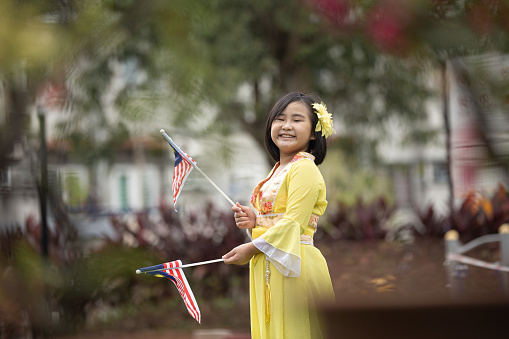 Asian Chinese girl with traditional clothes swinging national flag in public park