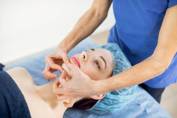 Relaxed young female client lying on couch while cosmetologist massaging her face