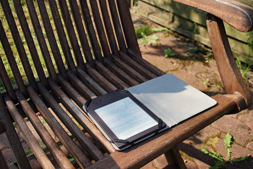 E-ink ebook reader lying on a wooden chair in the garden