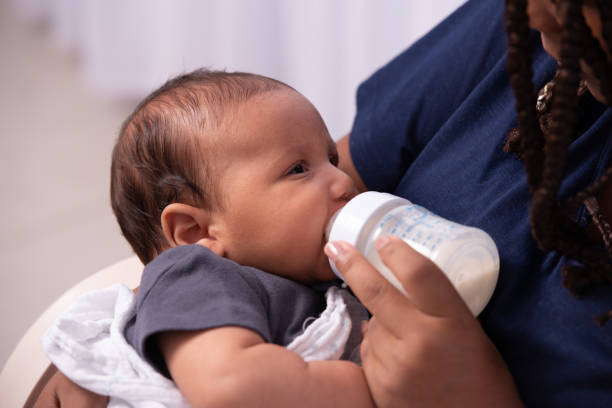 Shot of an adorable baby girl being bottle-fed milk at home by her mother. Close-up image of a loving mother feeding baby girl with the bottle at home. formula stock pictures, royalty-free photos & images