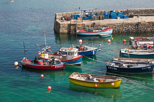 Coverack, Cornwall, UK - July 1, 2021.  The picturesque harbour and village of Coverack in Cornwall with small fishing boats moored on a turquoise ocean.