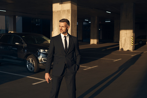 Confident mature man in full suit walking by parking lot