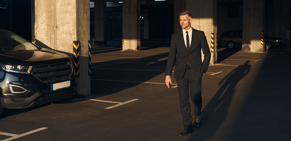 Full length of confident mature man in full suit walking by parking lot