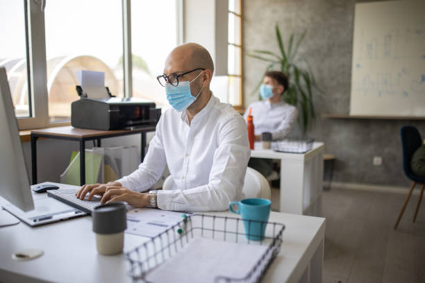 istock Businessman with protective face mask sitting at desk and working on computer in office 1334659809