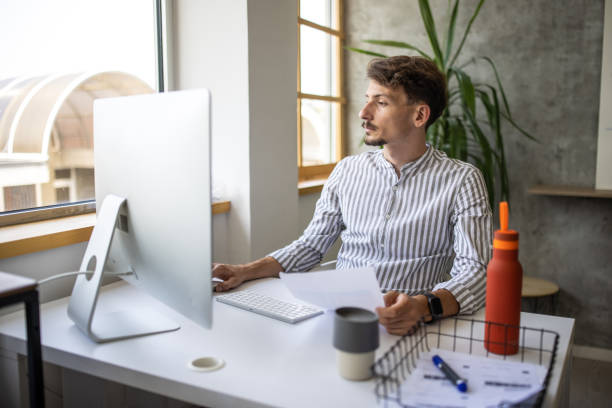 istock Young businessman sitting at desk and using computer in office 1334659888