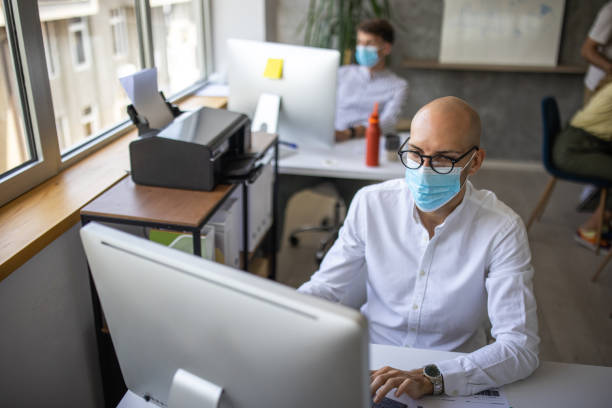 istock Businessman with protective face mask sitting at desk and working on computer in office 1334659892
